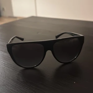 Michael Kors solglasögon leopardmönster - Snygga svarta solglasögon från Michael Kors, modell MK2111 Barrow. Bågarna har coolt leopardmönster och MK-logga i guld på sidorna. Stora, fyrkantiga glas och detaljer i svart och guld ger en riktigt trendig vibe.