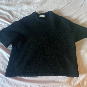 Svart stickad tröja från Gina Tricot - En svart stickad tröja med korta ärmar och rund hals. Tröjan har en loose passform och är gjord i ett mjukt material som passar perfekt för lager-på-lager. Enkel och stilren design som funkar till många outfits.