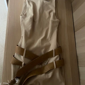 Beige kort klänning med bälten  - Superfräsch beige kort klänning från Zara med ärmlös design och två breda bruna bälten i midjan som unik detalj. Tight passform som framhäver figuren och stilren look. Helt oanvänd med prislappen kvar 🤍