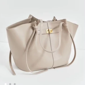 Beige axelväska från Gina Tricot - Stilren beige axelväska från Gina Tricot i slätt syntetmaterial. Väskan har en rymlig design med snörningsdetaljer på sidorna och ett snyggt guldfärgat spänne framtill. Invändigt finns en dragkedjeficka för småsaker. Perfekt för dig som gillar minimalistisk och trendig look. Slutsåld och som ny dock lite slitage på handtagen men de e verkligen inget som synns alls 