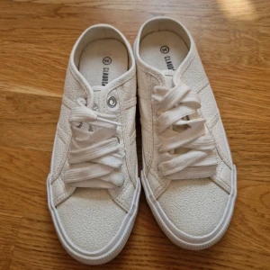 Vita sneakers från Claudia, strl 35 - Snygga vita sneakers från Claudia i storlek 36. Skorna har en klassisk design med rund tå, breda vita snören och en texturerad yta i syntetmaterial. Perfekta för dig som gillar en clean och enkel stil.
