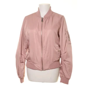 Rosa bomberjacka med dragkedja - Rosa bomberjacka med klassisk ribbad krage, muddar och midja. Jackan har dragkedja framtill och en extra ficka med zip på ärmen. Perfekt för dig som gillar en blandning av feminin och maskulin stil.