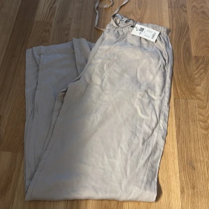 Beiga linnebyxor med dragsko - Snygga och luftiga beiga linnebyxor med dragsko i midjan. Perfekta för varma dagar och chill stil. Byxorna har raka ben och sidfickor för en avslappnad vibe.