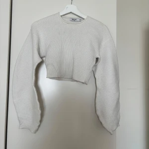 Vit croppad stickad tröja NA-KD - Superfin croppad tröja från NA-KD i vit färg. Tröjan är ribbstickad med långa, voluminösa ärmar och rund halsringning. Perfekt för lager-på-lager och ger en trendig vibe till din outfit. Finns några fläckar som borde gå bort i tvätt!