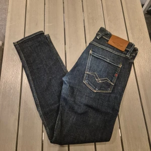 Replay Anbass jeans mörkblå tapered - Säljer ett par mörkblå Replay Anbass jeans med snygga kontrastsömmar och klassiska fem fickor. Jeansen har tapered passform och normal midja, vilket ger en modern och avslappnad look. Perfekta för dig som gillar stilrena och bekväma jeans. Jeansen är i ny skick använda mest 5 gånger.