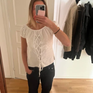 Vit blus med snörning och broderi - Supersöt vit blus med snörning framtill och broderade blommor på sidorna. Perfekt till sommar!! Jättefint skick också då den är sparsamt använd💖💖