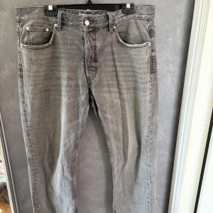 Grå jeans från Zara, rak modell - Säljer ett par grå jeans från Zara i rak passform. Jeansen har klassisk femficksdesign, knappgylf och snyggt tvättad finish. Materialet är robust denim i bomull och färgen är en schysst mellangrå ton som passar till det mesta.