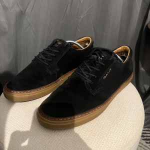 Svarta mockasneakers från Gant - Snygga svarta sneakers från Gant i mocka med mörkblå snörning och bruna gummisulor. 