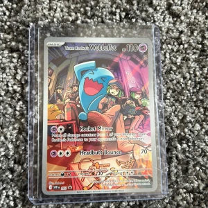 Team Rocket's Wobbuffet - Cool Pokémon-samlarbild med Team Rocket och Wobbuffet i färgstark design. Perfekt för dig som älskar Pokémon och vill utöka din samling med en unik och snygg kort. Kortet är skyddat i plastfodral och passar både nya och erfarna samlare.