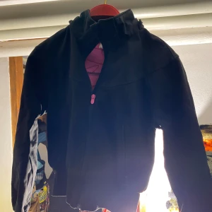 Svart fleecejacka med dragkedja - Svart fleecejacka med hög krage och rosa dragkedja framtill. Jackan har en enkel och stilren design, perfekt för lager-på-lager och chill dagar. Långärmad och mjuk, passar bra när det är lite kyligare ute.