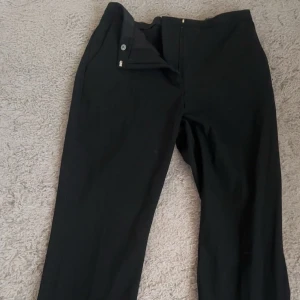 Svarta kostymbyxor från BikBok - Svarta kostymbyxor från BikBok i klassisk rak modell. Byxorna har dragkedja och knapp framtill och är perfekta för en clean och stilren look. Materialet känns mjukt och följsamt, vilket gör dem bekväma att bära hela dagen.