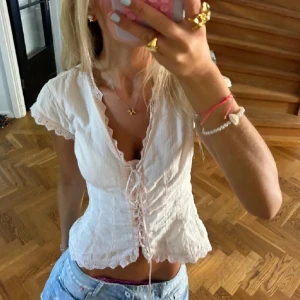 Vit blus med snörning och spets - Supersöt vit blus med v-ringning, snörning framtill och spetsdetaljer längs kanterna. Korta ärmar med volang och romantisk känsla. Perfekt till jeans eller kjol för en trendig look. Efterfrågad topp från hm!