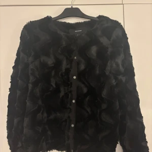 Svart pälsjacka från Vero Moda - Säljer en supermjuk och fluffig svart pälsjacka från Vero Moda. Den har långa ärmar och knäpps med knappar framtill. Perfekt för att hålla sig varm och stilren under kyliga dagar. Passar både till vardags och fest! Den är i storlek M och endast använd 3 gånger. Inga skador! Köparen står för frakten!