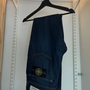 Stone Island mörkblå jeans - Säljer ett par mörkblå jeans från Stone Island med klassisk femficksdesign och ikoniska patchen på bakfickan. Jeansen har raka ben och snygga kontrastsömmar. Perfekta för dig som vill ha en clean och stilren look med streetkänsla.