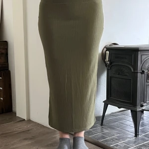 Olivgrön ribbad långkjol från Pieces - Säljer en olivgrön långkjol från Pieces i ribbad, stretchig polyester. Kjolen har en tight passform och är perfekt för dig som gillar en enkel men snygg look. Midjan är elastisk och materialet är mjukt mot huden. Med slits med till.