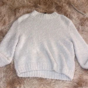Vit fluffig stickad tröja H&M Divided - Supermjuk och fluffig vit stickad tröja från H&M Divided. Tröjan har en rund halsringning, lång ärm och ribbade muddar. Perfekt för lager-på-lager och ger en cozy vibe till din outfit.