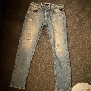 Replay ljusblå slitna jeans - Säljer ett par ljusblå jeans från Replay med snygga slitningar och distressed detaljer framtill. Klassisk femficksmodell med raka ben och normal passform. Jeansen har läderpatch bak i  midjan och är tillverkade i mjukt denimtyg. Modellen är Grover och storlekn är 33/32