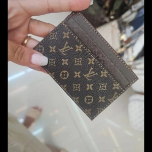 Brun kortfodral - Säljer ett stilrent kortfodral från  i klassiskt monogrammönster. Fodralet är brunt med LVloggor och har flera fack för kort. Perfekt att ha i fickan eller väskan för en lyxig touch.