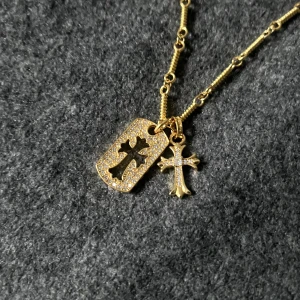Golden Rockstar Cutout Necklace - Kedjan (ca 55 cm) kan kortas eller fästas längs hela längden för flexibel passform. Tag: 2,6 cm, kors: 2 cm.