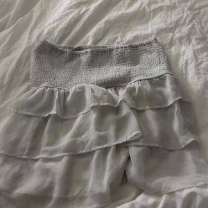 Vita volangshorts med smock - Superfina vita shorts med bred smock i midjan och flera lager volanger som ger en flowy och luftig känsla. Perfekta för varma dagar när du vill ha något både bekvämt och snyggt. Lätta och tunna i materialet, passar perfekt till sommarens outfits.