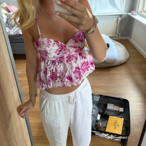 Blommig vit och rosa linnetopp - Supersöt linnetopp med tunna axelband och volangig nederdel. Toppen är vit med rosa blommigt mönster och har en lätt rynkad effekt över bysten. 