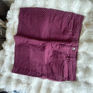Vinröda prickiga shorts med fickor - Snygg vinröd kjol med vita prickar och klassisk jeansmodell. Shortsen har både fram- och bakfickor, bälteshällor och knappstängning. Perfekta för dig som vill sticka ut med ett lekfullt mönster och cool färg. Passar till sommarens alla outfits!