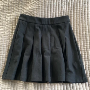 Svart plisserad kjol från Zara - Svart kortkjol från Zara med snygga plisserade veck. Kjolen har en klassisk midja och är tillverkad i en mjuk blandning av viskos och polyester med stretch. Perfekt för dig som gillar en elegant och clean kjol! 