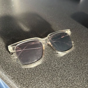 Transparenta solglasögon med fyrkantig båge - Säljer ett par trendiga solglasögon med transparent plastbåge och fyrkantig form. Glasen är mörka och ger en cool vibe till din look. Perfekta för att lyfta vilken outfit som helst.