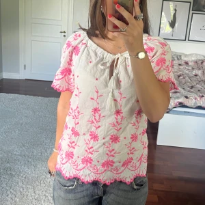 Vit blus med rosa broderi✨ - Supersöt vit blus från Next Petite med broderade blommor i starkt rosa. Blusen har korta ärmar, knytning med tofsar vid halsen och vågig kant nertill och vid ärmslut. Perfekt för en somrig look med jeans eller kjol. Tröjan är köpt begagnad men har inga synliga defekter💞