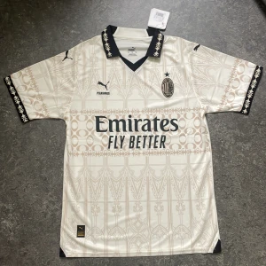AC Milan x Pleasures Bortatröja 2023/24 – Storlek M - Unik och limiterad AC Milan bortatröja säsongen 2023/24 i samarbete med Pleasures. Stilren beige design med gotiska detaljer och svart krage. Perfekt för både samlare och fotbollsfans som vill sticka ut med något ovanligt.  ✔️ AC Milan x Pleasures specialutgåva ✔️ Slim fit – storlek M ✔️ I Nytt skick , ej använd.