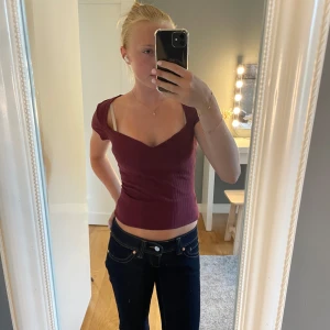 Vinröd ribbad croppad topp - Snygg vinröd croppad topp med v-ringning och korta ärmar. Toppen är ribbad och sitter tight, perfekt för dig som gillar en stilren men ändå trendig look. Passar till både jeans och kjol för en cool vibe.