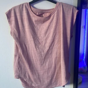 Rosa ärmlös topp från SOC - Säljer en ljusrosa ärmlös topp från SOC i mjuk och lätt polyester. Toppen har rund halsringning och en loose passform, perfekt för träning eller chill dagar. Enkel design med diskreta sömmar och något längre baktill.