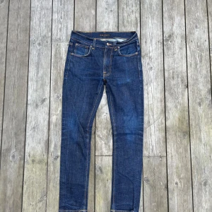 Mörkblå jeans från Nudie Jeans - Snygga mörkblå jeans från Nudie Jeans med klassisk femficksdesign och kontrastsömmar. Modellen har raka ben och ikoniska broderade bakfickor. Perfekta för dig som gillar stilrena och tidlösa jeans i kraftig denim.