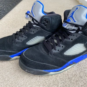 Nike Air Jordan 5 Retro blue svart/blå - Nike Air Jordan 5 Retro blue med svart mocka, blå detaljer och silvergrå plös med blå Jumpman-logga. Skorna har snörning, genomskinliga meshpaneler på sidorna och en cool blå sula. Perfekta för dig som vill sticka ut med en klassisk Jordan-stil. Skorna är i storlek 43. Nypris när jag köpte de var 3500 kr. 