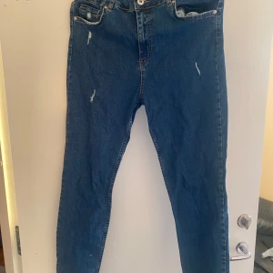 Blå skinny jeans från Koton, W32 L32 - Snygga blå skinny jeans från Koton med hög midja och slitna detaljer framtill. Klassisk femficksmodell med dragkedja och knapp. Jeansen är i stretchigt denim och har en smal passform som sitter tajt längs benen.