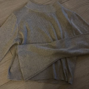 Grå ribbad polotröja S - Säljer en grå ribbad polotröja i storlek S. Tröjan har lång ärm, hög krage och är tillverkad i ett mjukt, stretchigt material.