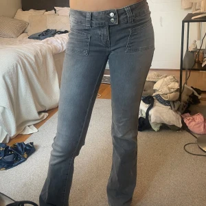 Grå bootcut jeans med fickor - Snygga grå jeans med bootcut-modell och två stora fickor framtill. Jeansen har låg midja, dubbla knappar och är tillverkade i ett mjukt bomullsmaterial med lite stretch. Perfekta för dig som gillar en avslappnad men trendig look.
