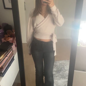 Ljusbeige omlott-tröja med knyt - Supersnygg ljusbeige omlott-tröja med knyt i midjan och v-ringad hals. Tröjan är croppad och har långa ärmar med ribbade muddar. Perfekt att styla med jeans eller kjol för en trendig look.