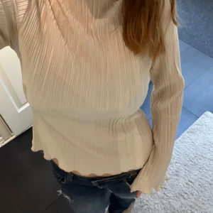 Plisserad beige långärmad topp - Säljer en beige plisserad topp med lång ärm och lätt utsvängda ärmslut. Toppen har en hög hals och vågig kant nertill,  köpt från MQ i storlek Xs💗