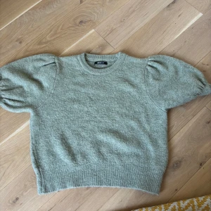 Grön stickad tröja med puffärm Gina Tricot - Superfin ljusgrön stickad tröja från Gina Tricot med korta puffärmar och rund hals. Tröjan har ribbade muddar och en mjuk, mysig känsla. Perfekt för dig som gillar en chill men ändå trendig look.