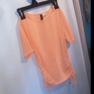 H&M - Crop top - Somrig korallfärgad crop top med snörning på vardera sida som man kan justera längden lite med. Har endast testats så den är nyskick. Storlek S. Erbjuder rabatt vid köp av 2 eller fler produkter! 