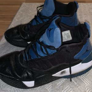 Svarta och blåa Jordan sneakers - Säljer ett par feta Jordan sneakers i svart och blått med coola detaljer och Jumpman-logga på tungan och hälen. Skorna har snörning, robust sula och är tillverkade i en mix av skinn och syntetmaterial. Perfekta för dig som gillar streetstyle och basketvibe.