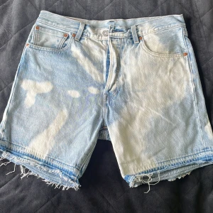 Levi's ljusblå jeansshorts med rå kant - Säljer ett par Levi's Premium jeansshorts i ljusblått med coolt blekta detaljer och rå, fransig kant nertill. Klassisk femficksmodell i 100% bomull, perfekt för en avslappnad stil. Shortsen har normal passform och midja.