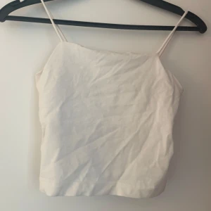 Vit linnetopp med smala axelband - Enkel och stilren vit linnetopp med smala axelband. Toppen har rak passform och ärmlös design, perfekt för varma dagar. Tidlös och lätt att matcha med olika outfits.