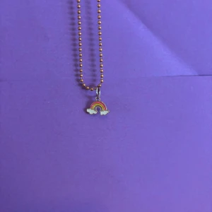 Halsband med regnbågsberlock - Ett sött halsband med kulkedja i guldton och en liten regnbågsberlock med moln. Berlocken har färgerna röd, orange, gul, grön och blå samt vita moln. Perfekt för dig som gillar färgglada detaljer och vill sticka ut lite extra.