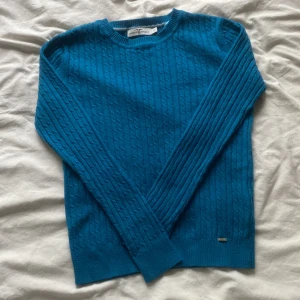 Blå kabelstickad tröja Hampton Republic - Snygg blå kabelstickad tröja från Hampton Republic i storlek XS. Tröjan har rund halsringning, ribbade muddar och en liten metallbricka nertill. Perfekt för dig som gillar klassisk stil med en twist. Den är nästan orörd!!
