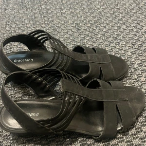Svarta sandaler med klack från Graceland - Svarta sandaler från Graceland med breda remmar och flera tunna remmar på sidorna. Skorna har en låg klack och öppen tå, perfekt för varma dagar. Snygg och enkel design som passar till många outfits. Skorna är 40, men däremot passar för 39. De är bekväma och faktiskt lätt och gå med.