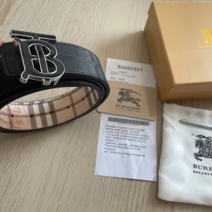 Burberry bälte - Snyggt Burberry bälte. Ena sidan är svart med klassiskt rutmönster och präglad logga, andra sidan har Burberrys beigea rutor med bruna och röda detaljer. Bältet är gjort i skinn och levereras med originalbox, kvitto och dustbag.