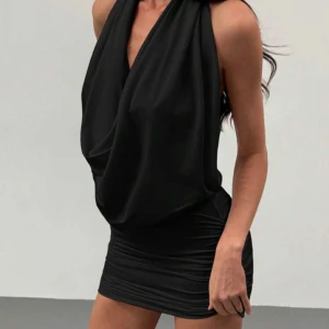 Svart kort klänning med drapering - Snygg svart kortklänning med draperad framsida och djup v-ringning. Klänningen är ärmlös och har en tight passform nertill, perfekt för dig som vill sticka ut. Materialet känns mjukt och följsamt mot kroppen. Aldrig kommit till användning. Köpt på shein för 130 kr