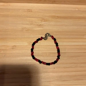 Svart och rött pärlarmband - Ett handgjort armband med små svarta och röda pärlor i ett enkelt, stilrent mönster. Armbandet har en metallfärgad låsdetalj och passar perfekt för dig som gillar färgstarka accessoarer med en personlig touch.